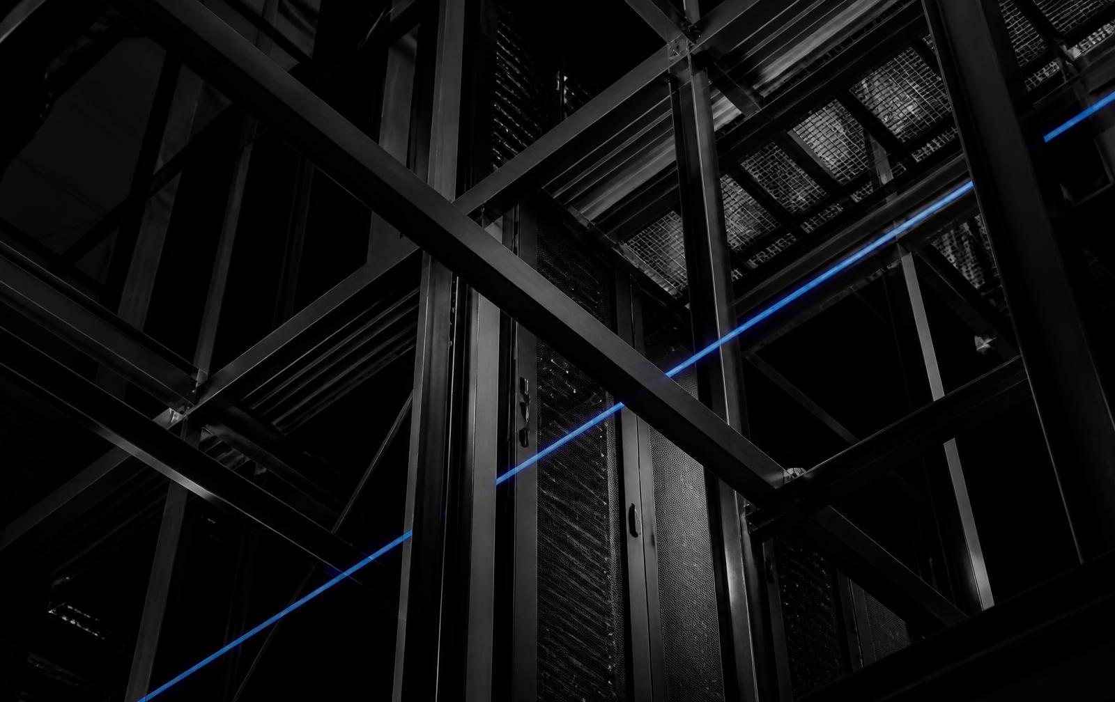 Steel structural framework above dark server cabinets, crossed by a single electric-blue light line